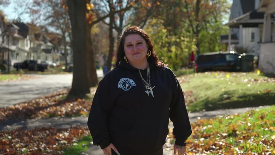 Woman in black hoodie standing on a residential street.