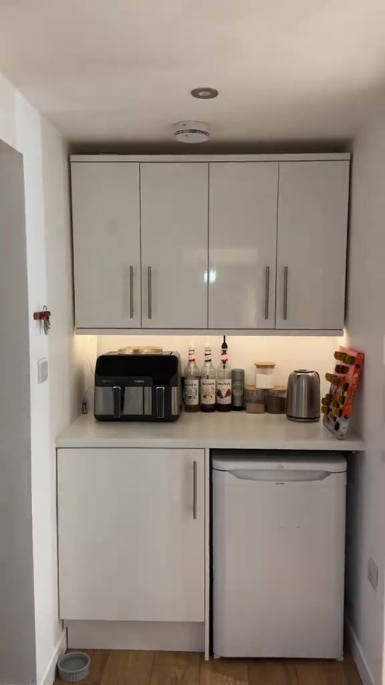 Tiny home kitchen area with white cabinets, appliances, and a small refrigerator.