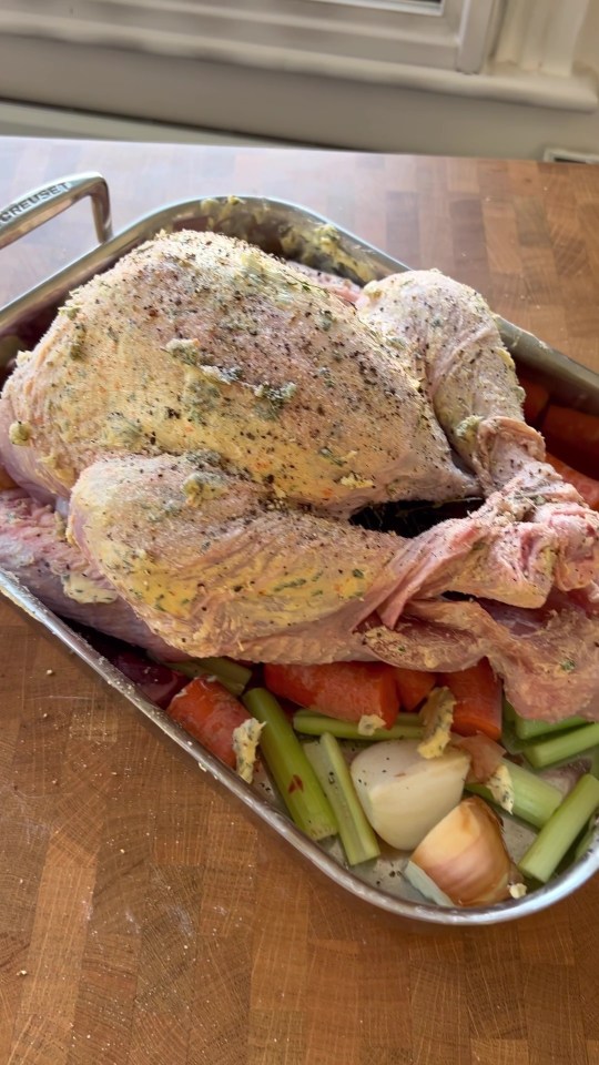 Buttered and seasoned turkey in a roasting pan with carrots, celery, and onion.