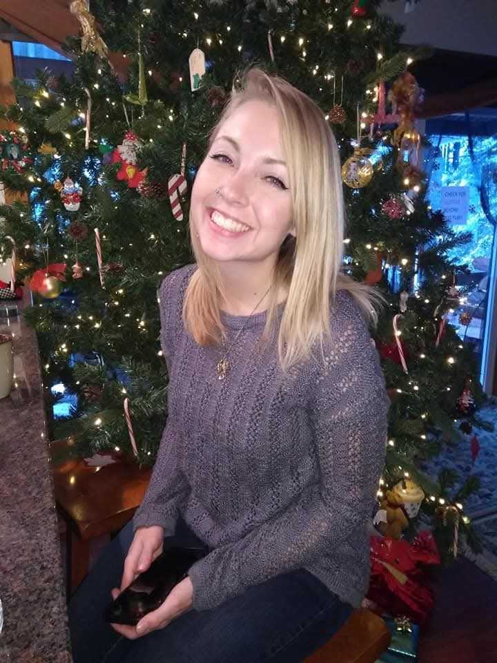 Woman smiling next to a decorated Christmas tree.