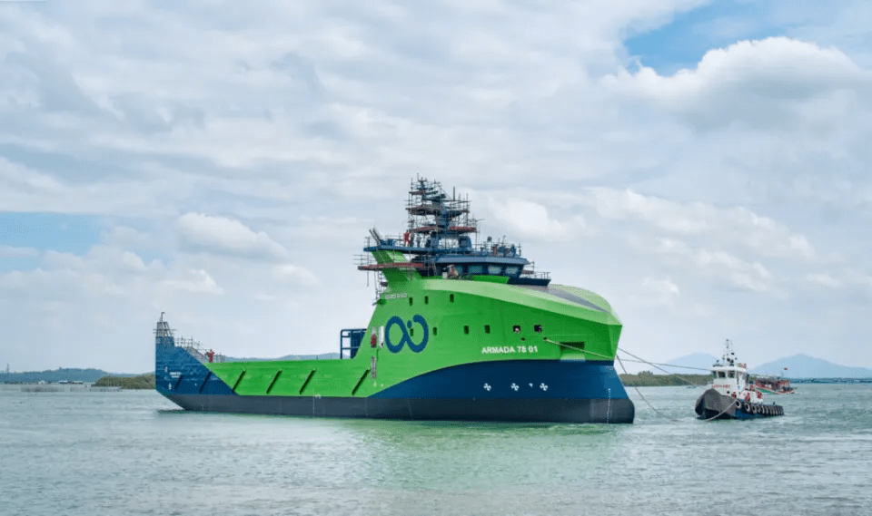 A green and blue Armada T8-01 ship being towed by a smaller tugboat.