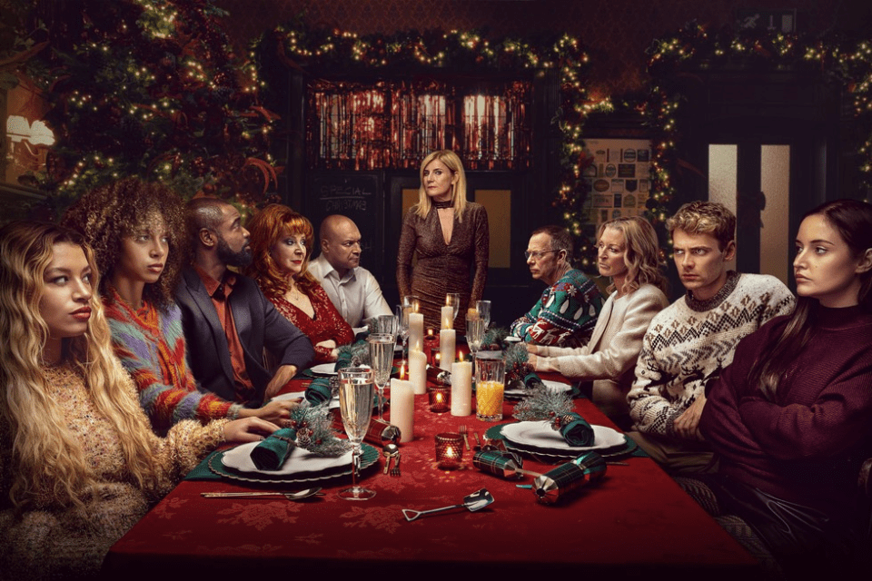 A large group of people sits around a Christmas dinner table, appearing tense.