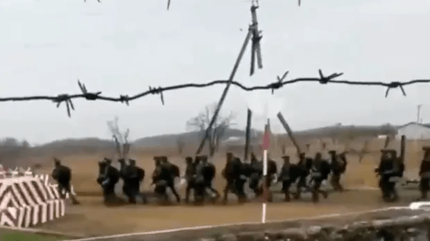 Soldiers running past a barbed wire fence.