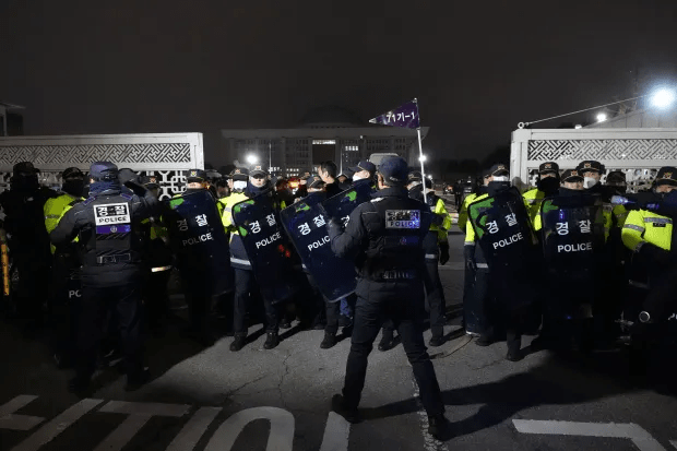 Police officers stand guard as the furious crowds try to get through the main gate