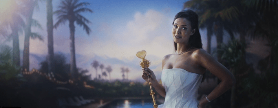 Woman in white strapless dress holding ornate scepter, tropical setting.