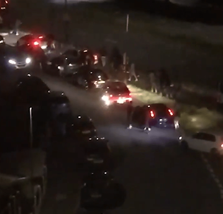 Nighttime street scene with cars and people gathered.