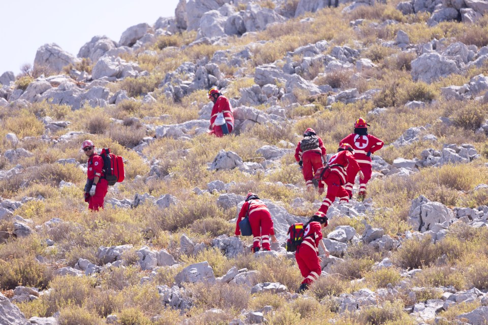 Red Cross rescue workers ascending a rocky hillside.