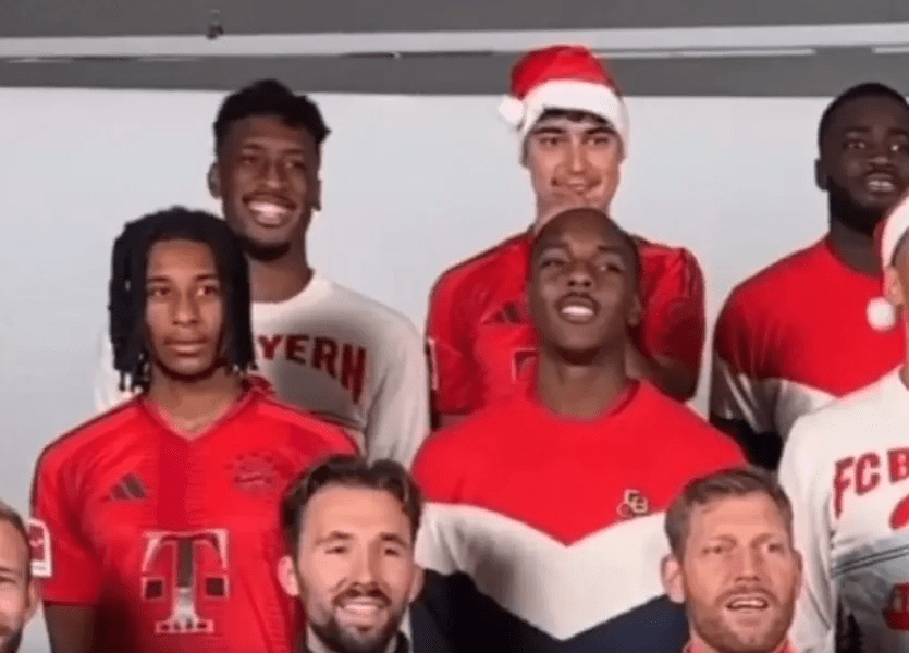 Group photo of Bayern Munich soccer players wearing red jerseys, some wearing Santa hats.