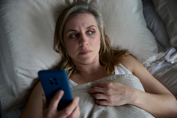 Menopausal woman in bed looking at her phone.