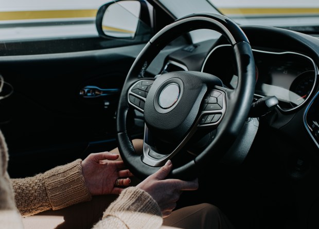 Person's hands gripping a black car steering wheel.