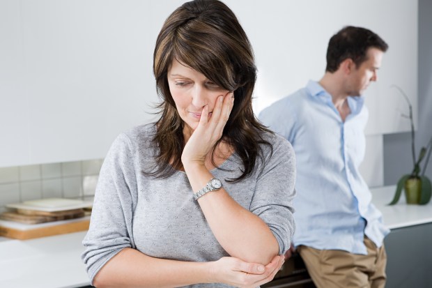 A couple ignoring each other in a kitchen.