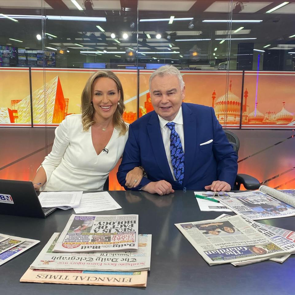 Two news anchors sit at a desk with newspapers.