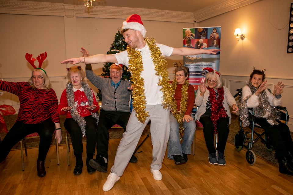 Actor leading seated seniors in a Christmas dance lesson.