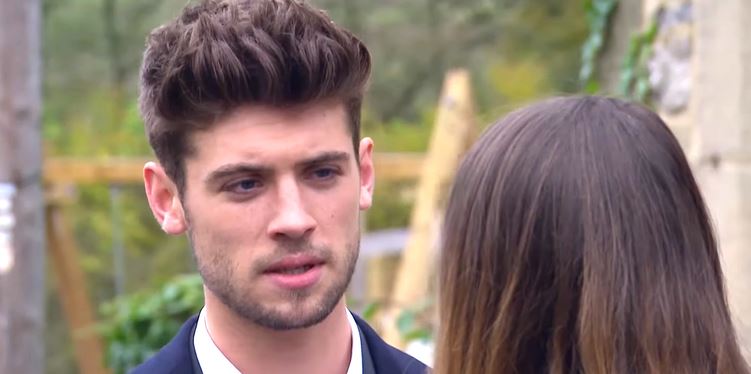 A man with dark hair looks concerned as a woman stands behind him.