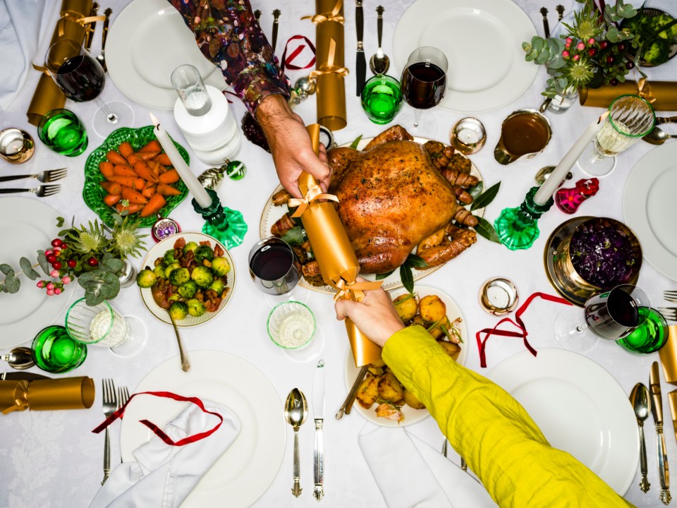 Overhead view of two people pulling a Christmas cracker at a festive dinner table.