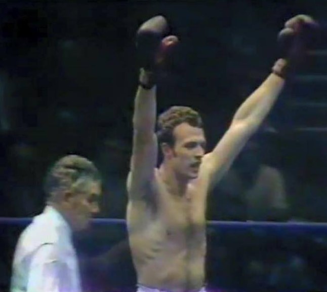 Neil Malpass, victorious boxer, raises his arms.