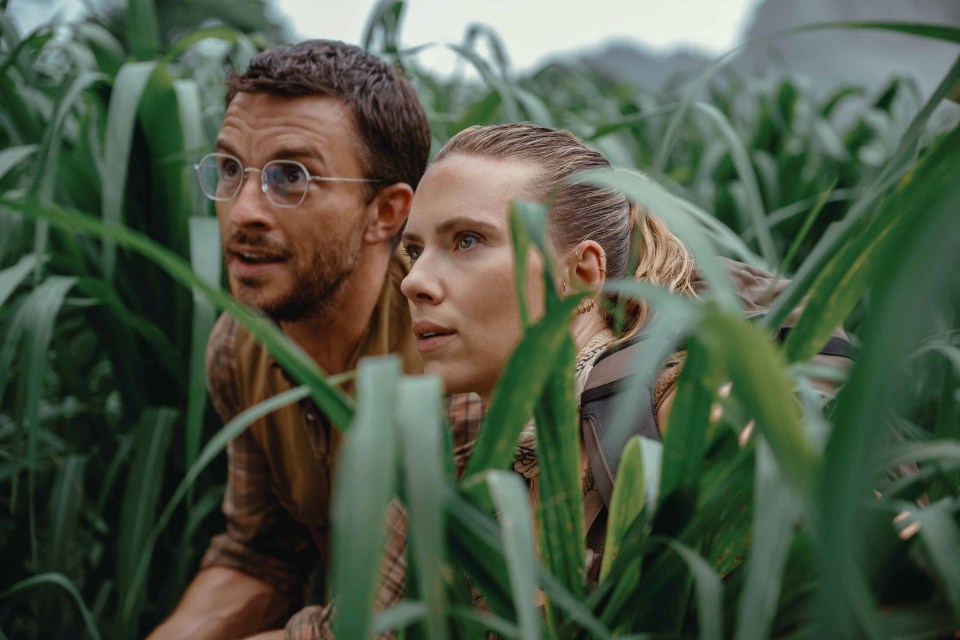 Jonathan Bailey and Scarlett Johansson hiding in tall grass.