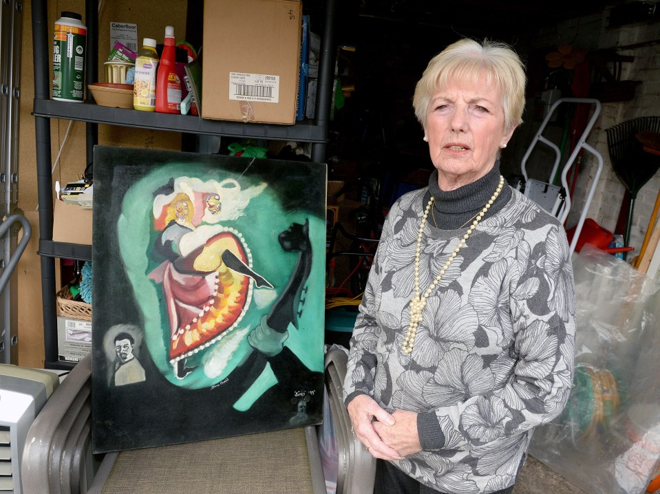 A woman stands in her garage next to a painting by the murderer of her daughter.