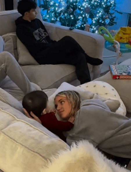 A woman and baby cuddle on a couch, while a teenager sits on another couch nearby.