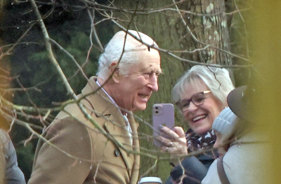 King Charles III smiles as a woman takes a photo of him.