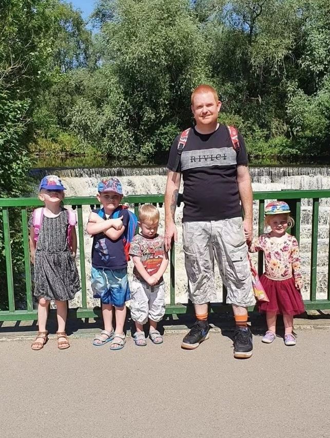 A father and his four young children stand on a bridge in front of a waterfall.