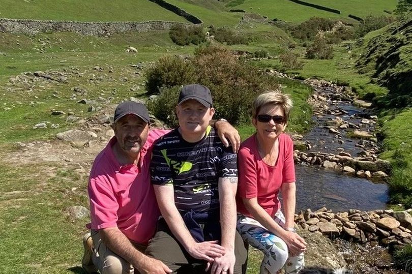 A man sits between his parents in a scenic outdoor setting.