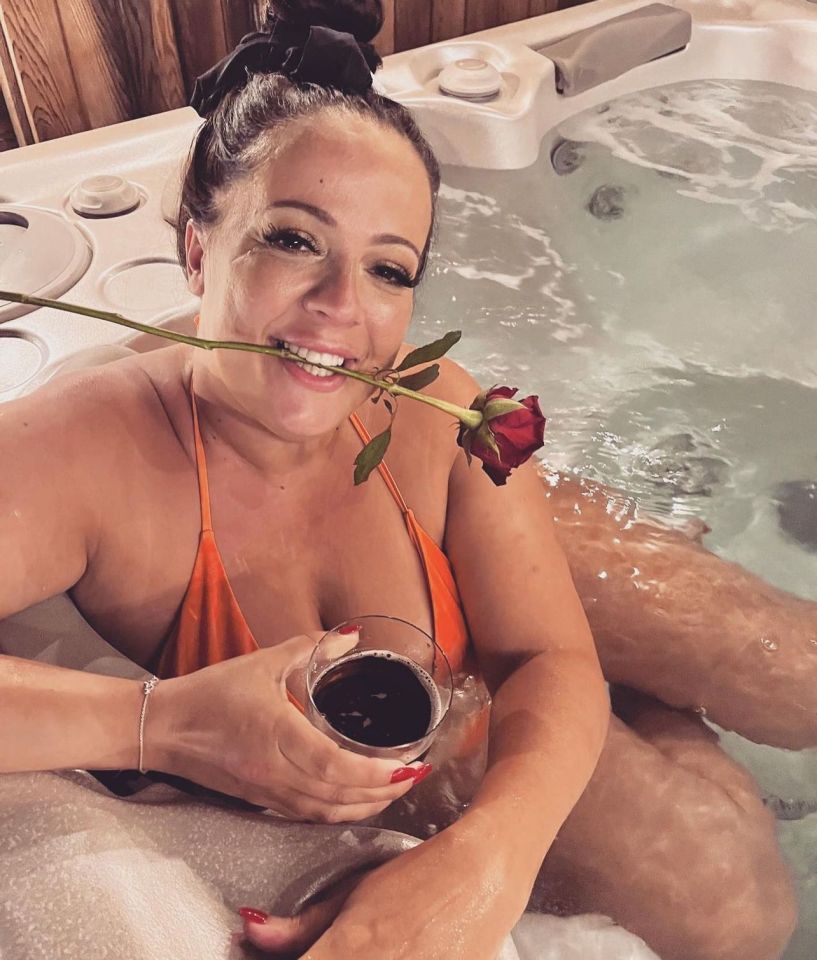 Woman in a hot tub holding a rose and a drink.