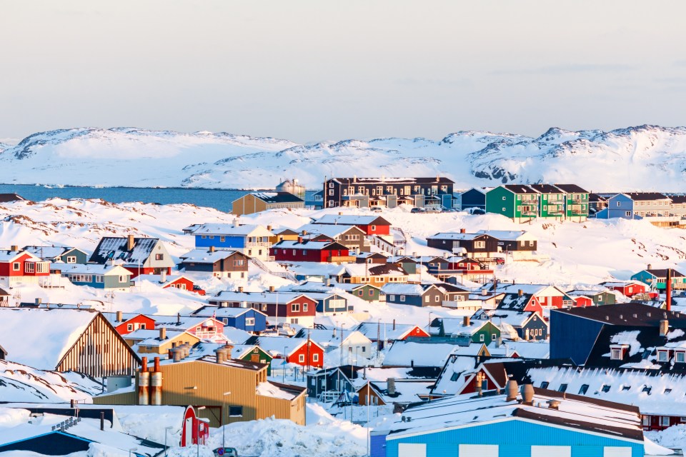 Snow-covered Inuit houses in Nuuk, Greenland, with mountains and sea in the background.