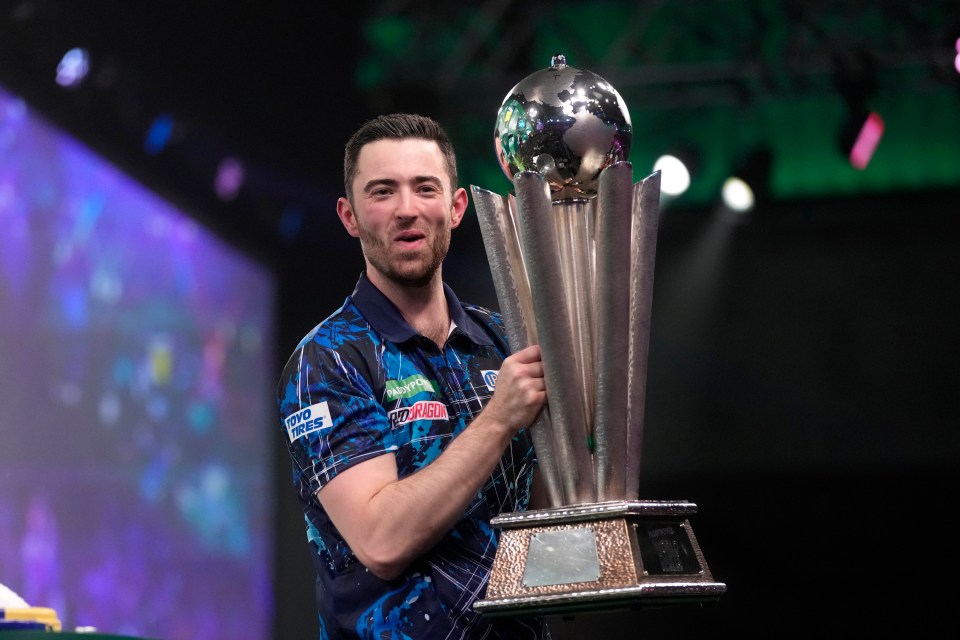 Luke Littler holding a darts trophy.