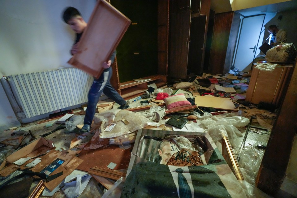 A looter walks by a broken portrait of the late Syrian President Hafez Assad in the palace