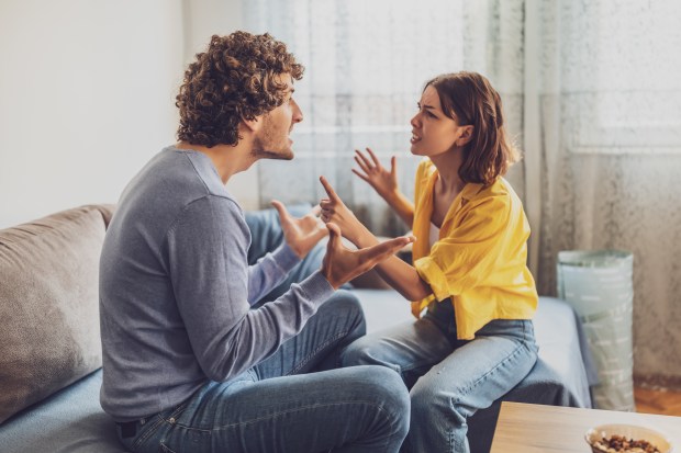 A young couple sits on a couch and argues.