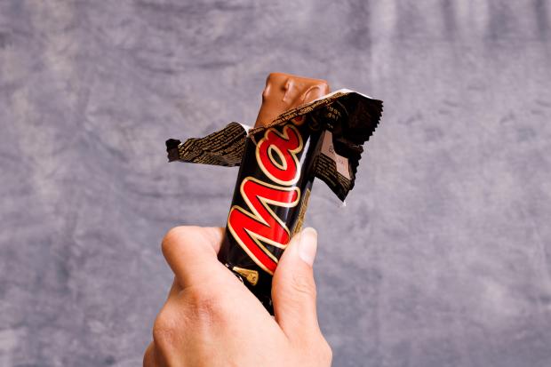 Hand holding an unwrapped Mars chocolate bar.