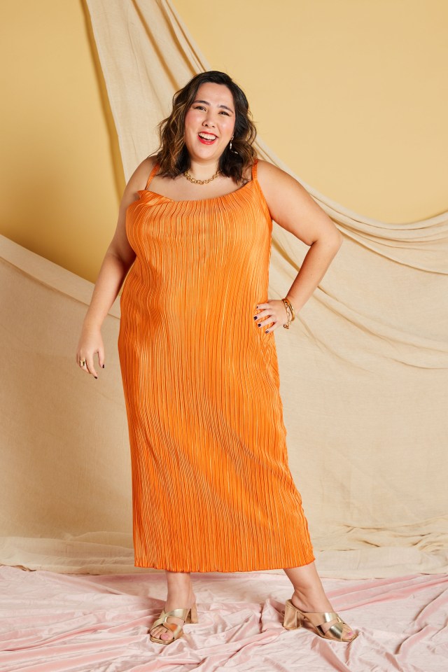 Woman in orange pleated maxi dress and gold heels.