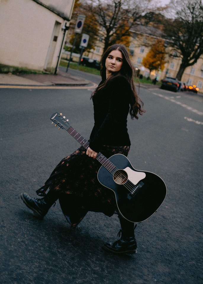 A woman walking down a street carrying a guitar.