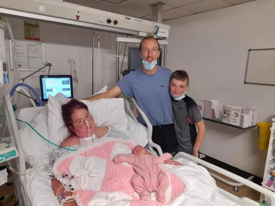 A mother recovering in a hospital bed with her newborn baby girl, her husband, and older son.