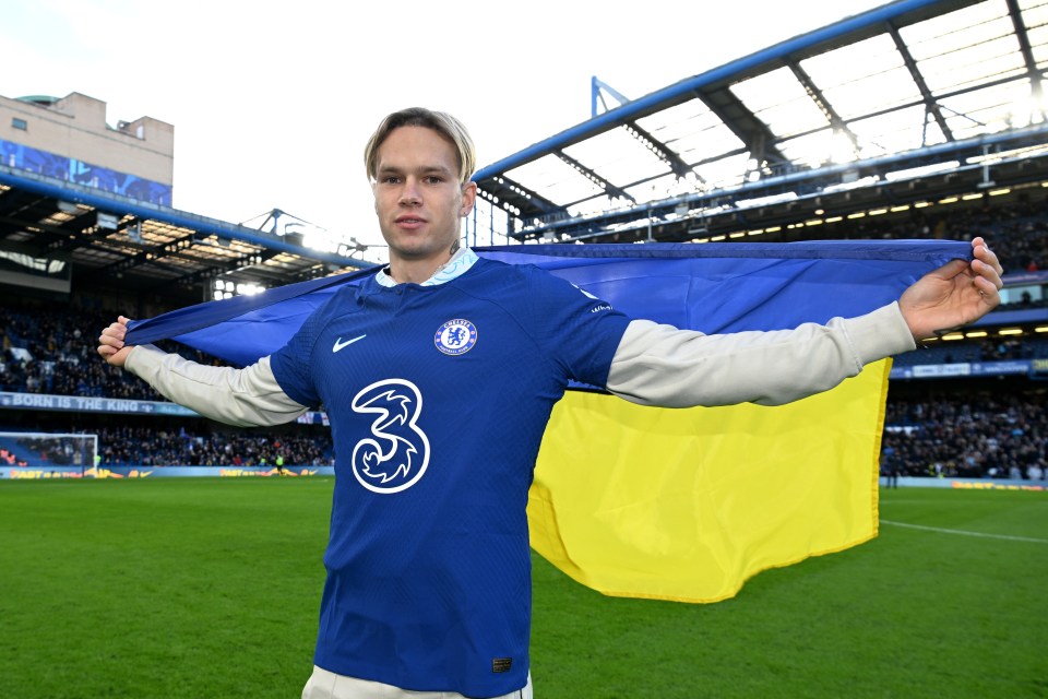 Mykhaylo Mudryk, new Chelsea F.C. signing, holding a Ukrainian flag at Stamford Bridge.