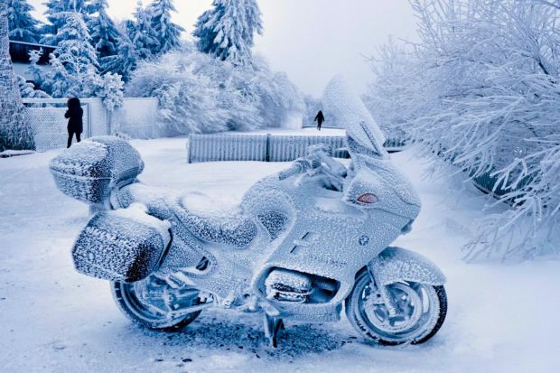 A snow-covered motorcycle parked in a snowy landscape.