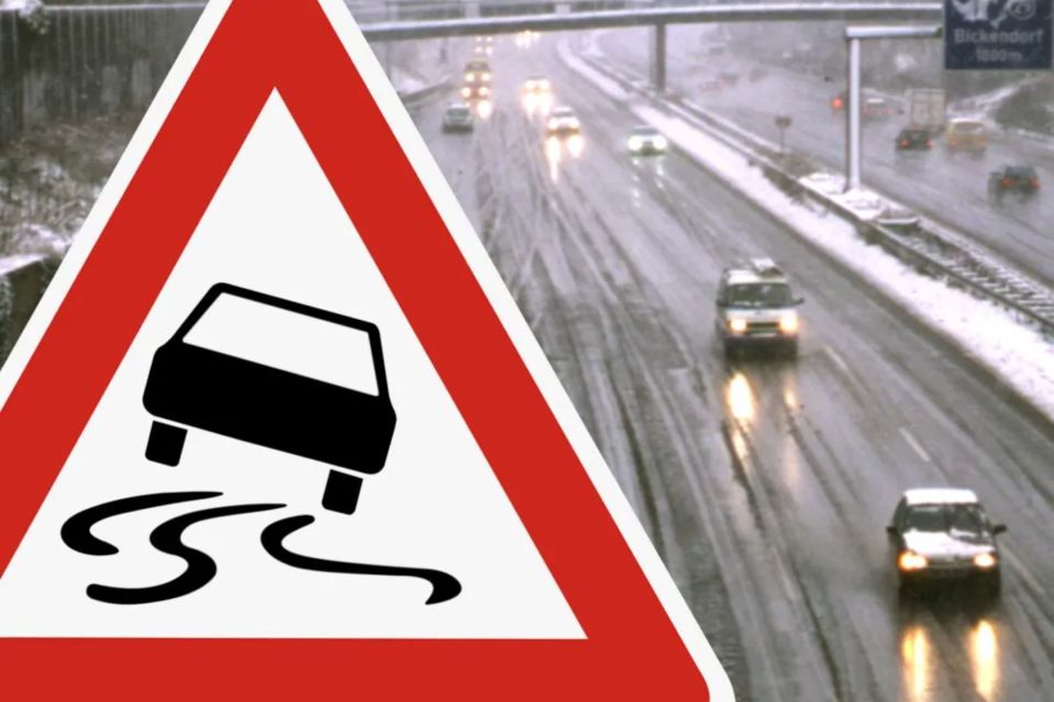 Slippery road warning sign with cars driving on a snowy highway.