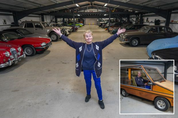 Woman standing in a large garage filled with classic cars, with a small wooden car in the inset.