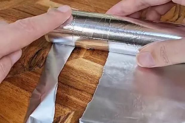 Hands rolling aluminum foil into a cylinder.