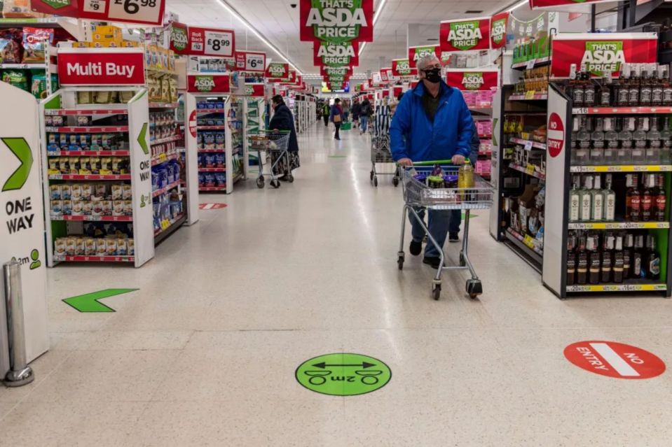 Shopper in an ASDA supermarket wearing a face mask.  Social distancing markers are on the floor.