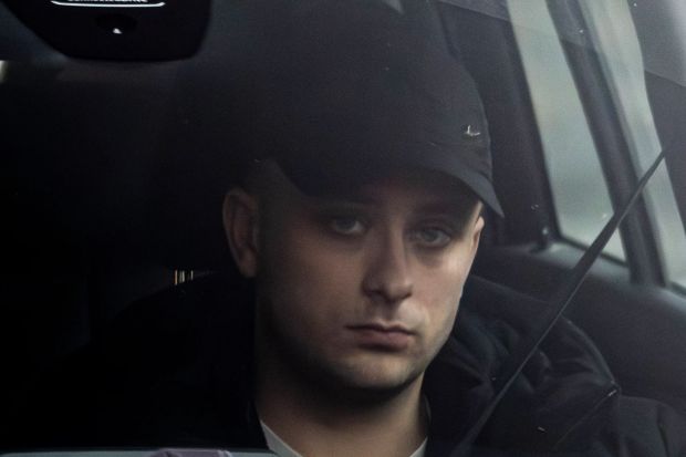 Close-up of a young man wearing a black baseball cap, sitting in a car.