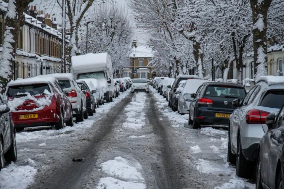 Snow-covered cars parked on a residential street.