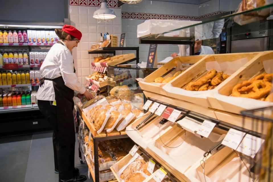 A bakery employee stocking shelves filled with various breads and pastries.