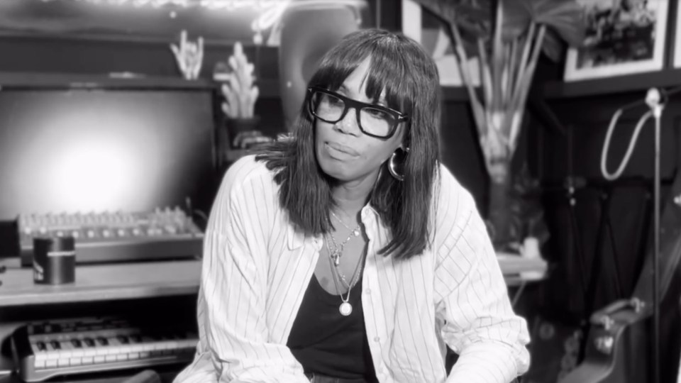 Black and white photo of a woman wearing glasses and a striped shirt, sitting in a recording studio.