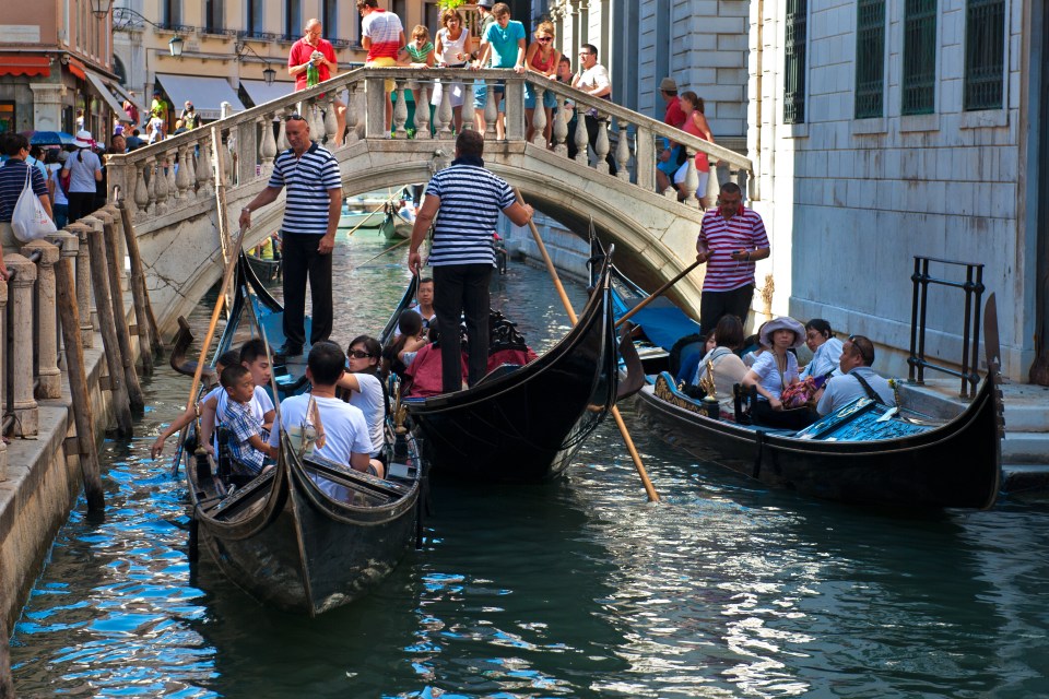 Gondolas on a Venetian canal with passengers and gondoliers.