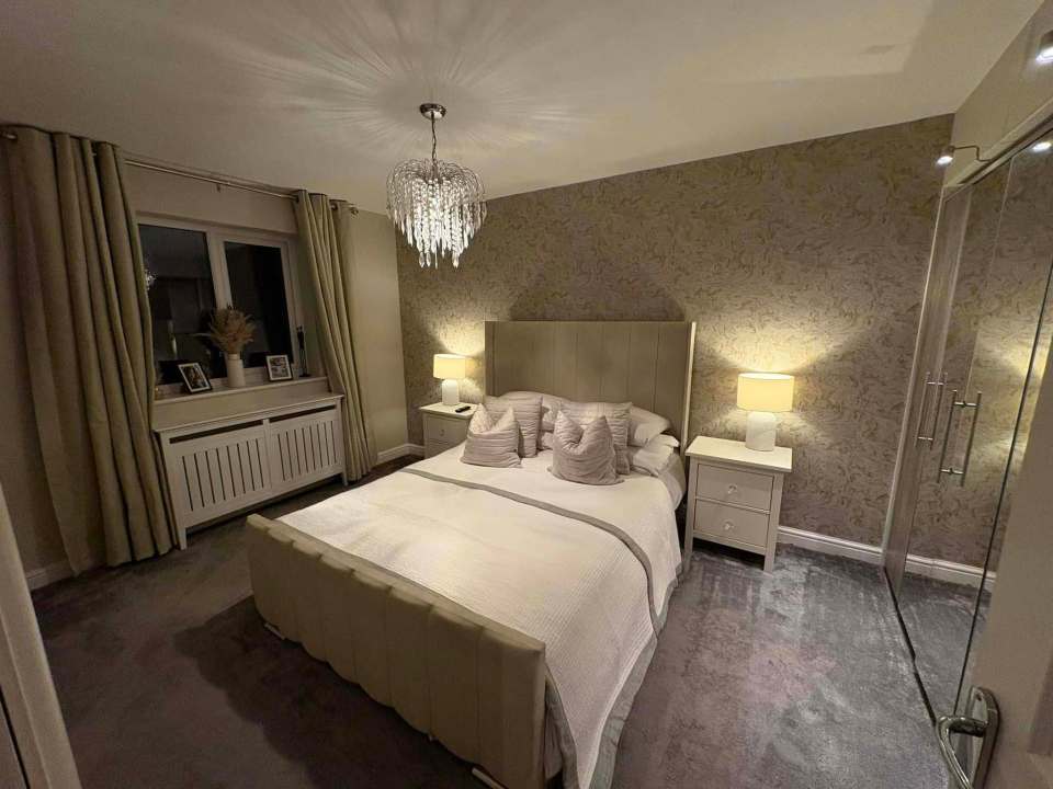 A transformed bedroom with a beige upholstered bed, neutral decor, and a crystal chandelier.