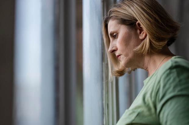 A woman looks sadly out a window.