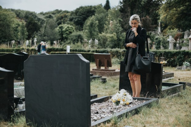 A grieving widow stands at her husband's grave.