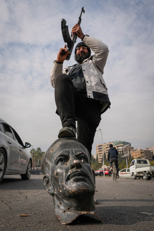 An opposition fighter steps on a broken bust of the late Syrian President Hafez Assad